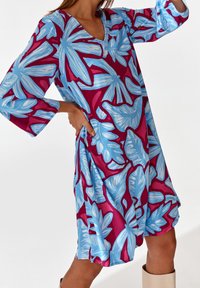 V-pääntie mekko, jossa on kolme neljäsosaa hihat, rohkealla sinisen ja burgundin kukkapainatuksella, valmistettu kevyestä kankaasta, jossa on lennokas muotoilu.