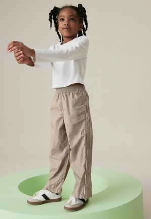 Top corto de manga larga blanco, pantalones beige de cintura elástica con detalles de botones en los lados, y zapatillas blancas con detalle de raya negra.