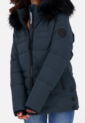 Marineblauwe gewatteerde jas met zwarte nepbontkraag, ritssluiting aan de voorkant, details met knopen aan de zijkant en een zak met ritssluiting, gecombineerd met een blauwe spijkerbroek.