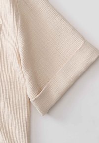 Manche courte de couleur crème avec un motif quadrillé texturé et un revers plié sur un fond clair uni.