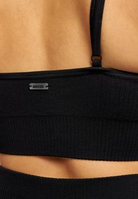 Bralette noir côtelé affichant une texture lisse avec des bretelles réglables et un petit logo métallique à l'arrière.