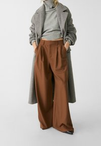 Hnědé široké kalhoty s puky, spojené s šedým rolákem a dlouhým šedým kabátem. Vyznačují se texturovanou tkaninou a uvolněným střihem.