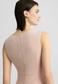 Bezramenné pastelově růžové šaty s vysokým výstřihem, zadním zipem a hladkým povrchem. Mají přiléhavý střih pro elegantní vzhled.