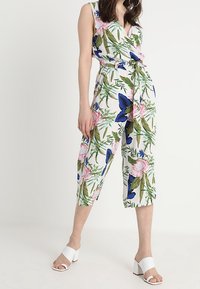 Jumpsuit floral con base blanca, hojas verdes y flores rosas con acentos azules. Diseño de escote en V con cintura ceñida y piernas recortadas.