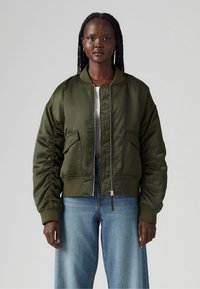 Olive green bomber jacket with a zip front, ribbed cuffs, and two front pockets. Smooth satin texture with a cropped design.