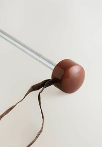 Ruskea kumikahva hopeisella metalliputkella, johon on kiinnitetty ruskea nauha. Kahva on pyöreä ja kiiltävä, mikä luo kontrastin tekstuurin omaavan nauhan kanssa.