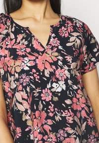 Krátký rukáv květinový top v námořnické modré s růžovými a krémovými květy; design s výstřihem do V; měkká tkanina s uvolněným střihem a jemnou texturou.