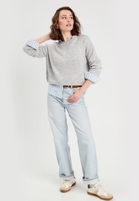 Un pull en maille gris à col rond sur une chemise rayée bleue et blanche, associé à un jean en denim bleu clair et des baskets blanches.