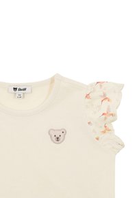 Camiseta de manga corta color crema con un bordado de oso en el pecho y mangas con volantes de patrón floral en tonos rosa y amarillo.