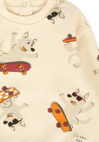 Felpa beige con divertenti cani dei cartoni animati su skateboard. I dettagli includono occhiali da sole, un tessuto testurizzato e un'etichetta cucita con la scritta "Sono un ragazzo figo."