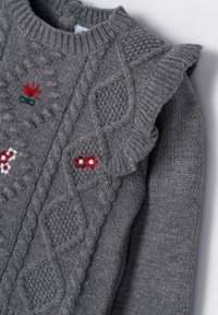 Grå stickad tröja med kabelmönster, liten röd och vit blommig broderi och volangdetaljer på axlarna.