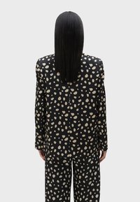 Crni odijelo s bež apstraktnim točkicama, uključuje krojenu jaknu i odgovarajuće hlače. Glatka tkanina sa strukturiranim dizajnom i dugim rukavima.