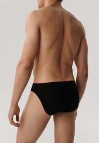 Czarne bawełniane majtki w fasonie slipów o gładkiej strukturze, z elastycznym pasem w talii i minimalistycznym designie, pokazane z widoku tylniego.
