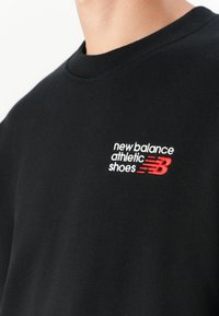 Black cotton sweatshirt with a ribbed crew neck. Features white and red embroidered text: "new balance athletic shoes" with a red logo accent.