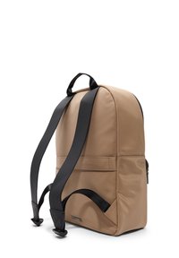 Sac à dos en nylon beige de forme arrondie, avec des bretelles en synthétique noires et une poche avant. Il dispose d'une poignée sur le dessus et d'une texture lisse.