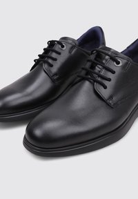 Zapatos de vestir de cuero negro con acabado suave, diseño de cordones, punta redondeada y suela texturizada. El interior presenta un forro azul oscuro.