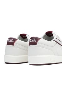 Sneaker bianche Vans con accenti bordeaux, dotate di pelle liscia, punta rotonda, design a profilo basso e dettagli di cucitura sul tallone.