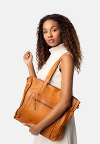 Sac fourre-tout en cuir orange chaud avec plusieurs poches, des bretelles et une surface texturée. Comprend un compartiment zippé et des lignes épurées.