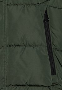 Mörkgrön puffjacka med horisontell quiltad sömnad, med en sidodetalj i svart dragkedja och en slät nylontextur.