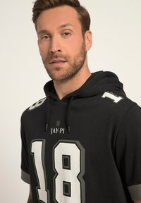 Felpa nera con cappuccio e dettagli in bianco e grigio. Presenta grandi numeri "18" e "1" sul davanti e un logo sopra. Tessuto in cotone, vestibilità casual.