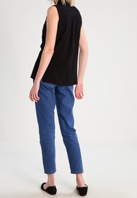 Haut noir sans manches avec col, présentant un design fluide. Associé à un jean bleu taille haute et des chaussures plates noires.