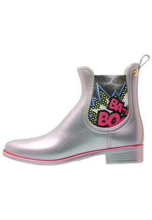 Botte de pluie argentée à la cheville avec bordure rose, panneau latéral élastique comportant un texte "BA-BOOM" coloré de style bande dessinée et un dessin graphique.