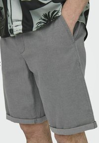 Shorts gri și texturat cu un model țesut, având buzunare laterale și tivuri răsucite. Asortați cu o cămașă cu un model alb și negru.