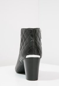 Bottine en cuir noir avec un motif matelassé, fermeture éclair et un talon épais. Présente un accent logo en argent sur le talon.