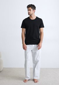 T-shirt en coton noir associé à un pantalon de pyjama rayé blanc et bleu clair, offrant une coupe décontractée et une texture douce.