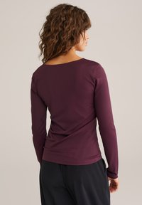 Bordo ilga rankovė viršutinė dalis, pagaminta iš lygios medžiagos, su plačiu iškirpimu ir laisvu siluetu, kartu su laisvomis juodomis kelnėmis.