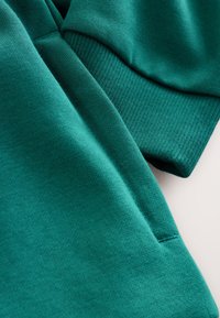 Tirkizna tkanina za majicu s mekanom teksturom, s rebrastim manžetama i glatkom površinom tijela. Jednostavan dizajn bez uzoraka ili ukrasa.