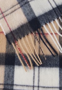 Wollen sjaal in een beige, zwart en witte geblokte patroon met rode accenten en franjes aan de randen. Zachte textuur met zichtbare weving.