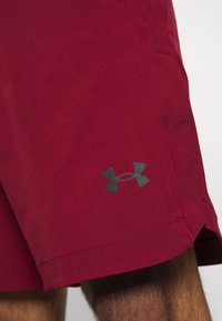 Pantalones cortos atléticos rojos hechos de tela transpirable, con una cinturilla elástica y un logo negro en la parte inferior izquierda.