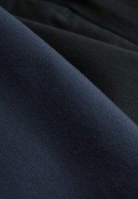 Nahaufnahme von glat gefaltetem Stoff mit sichtbarer Textur in dunkelblau und schwarz.