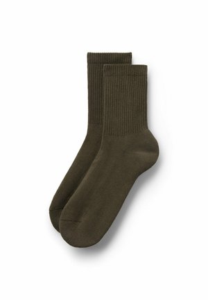 Paire de chaussettes montantes côtelées vert olive disposées à plat avec les bords en haut, sur un fond blanc.