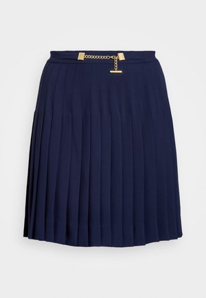 Jupe plissée bleu marine avec un détail de chaîne dorée à la taille, présentée sur un fond clair uni.