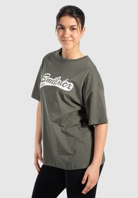 Camiseta de algodón verde oliva con mangas cortas, que presenta el texto en cursiva blanca "Smilthox" en la parte frontal. Cuello redondo, corte relajado.