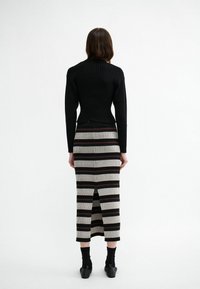 Schwarzer gerippter Rollkragenpullover und taillierter Midiskirt mit horizontalen beigen, schwarzen und burgunderfarbenen Streifen; Schlitz in der Mitte hinten; knöchellang mit schwarzen Socken.