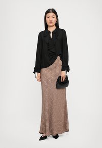 Black chiffon blouse with ruffled detailing, paired with a long brown plaid skirt. Black faux leather bag and pointed black flats complete the look.