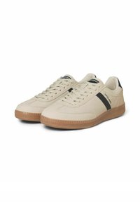 Baskets de sport beiges avec un dessus texturé, détail de bande noire et semelle en caoutchouc naturel. Présentent des lacets plats et un minimalisme dans le branding.