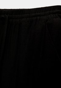 Pantalones con cintura elástica negra de tejido texturizado, que cuentan con bolsillos laterales y un ajuste relajado. La superficie está ligeramente arrugada.