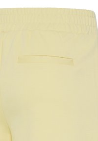 Pantalon en tissu jaune clair avec une taille élastique et une poche horizontale fendue à l'arrière sur le côté droit.