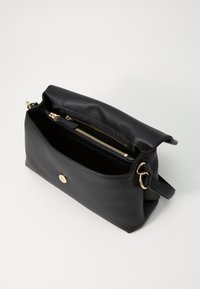 Bolso de cuero negro con interior con cremallera. Presenta herrajes dorados, un cierre de botón y una textura suave. Forma rectangular compacta.