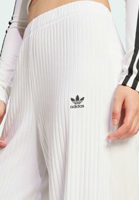 Vita ribbade byxor med elastisk midja och subtil adidas-logotyp i svart. Slät textur med vertikala linjer för en strukturerad look.