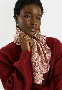 Écharpe légère en soie à fleurs couleur crème imprimée de motifs botaniques bordeaux, nouée autour du cou ; associée à un pull en maille bordeaux confortable.