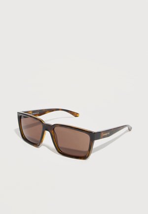 Obdĺžnikové slnečné okuliare s motívom korytnačky so sivohnedými šošovkami a štíhlymi ramenami, naklonené na bielom povrchu.