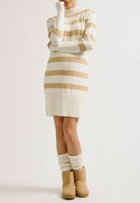 Robe pull rayée crème et beige avec ourlet côtelé et col montant, associée à des chaussettes crème côtelées et des bottines beige à la cheville.