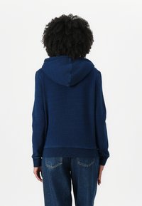 Sweatshirt à capuche bleu marine avec une finition texturée, poche kangourou et poignets côtelés ; associé à un jean en denim ample.