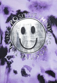 Fialové tričko s tie-dye vzorem, které obsahuje velkou stříbrnou grafiku smajlíka a text "POZITIVNÍ MYŠLENÍ" uspořádaný do kruhu.