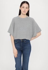 Maglione corto grigio chiaro con scollo rotondo e maniche corte, realizzato in tessuto morbido. Abbinato a jeans in denim blu.